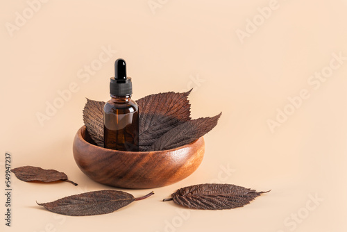 anti-aging serum or cosmetic in a glass bottle with a pipette in a wooden bowl with brown leaves on a beige background. front view.