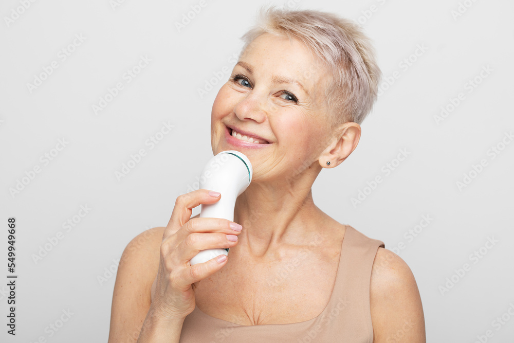 Beauty face portrait of cute and pretty senior woman with short hair using facial massager for perfect fresh skin Beauty face portrait of cute and pretty senior woman with short hair using facial massager for perfect fresh skin