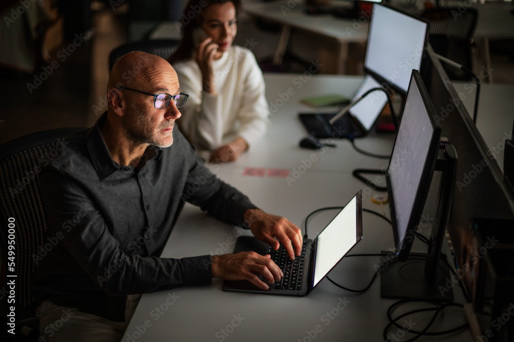 Tired businessman working on computer in office in late evening with him female colleague Tired businessman working on computer in office in late evening with him female colleague