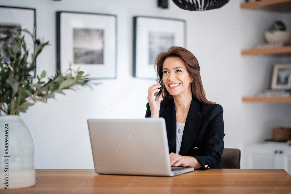Attractive middle aged woman wearing blazer and making a call while working at home Attractive middle aged woman wearing blazer and making a call while working at home