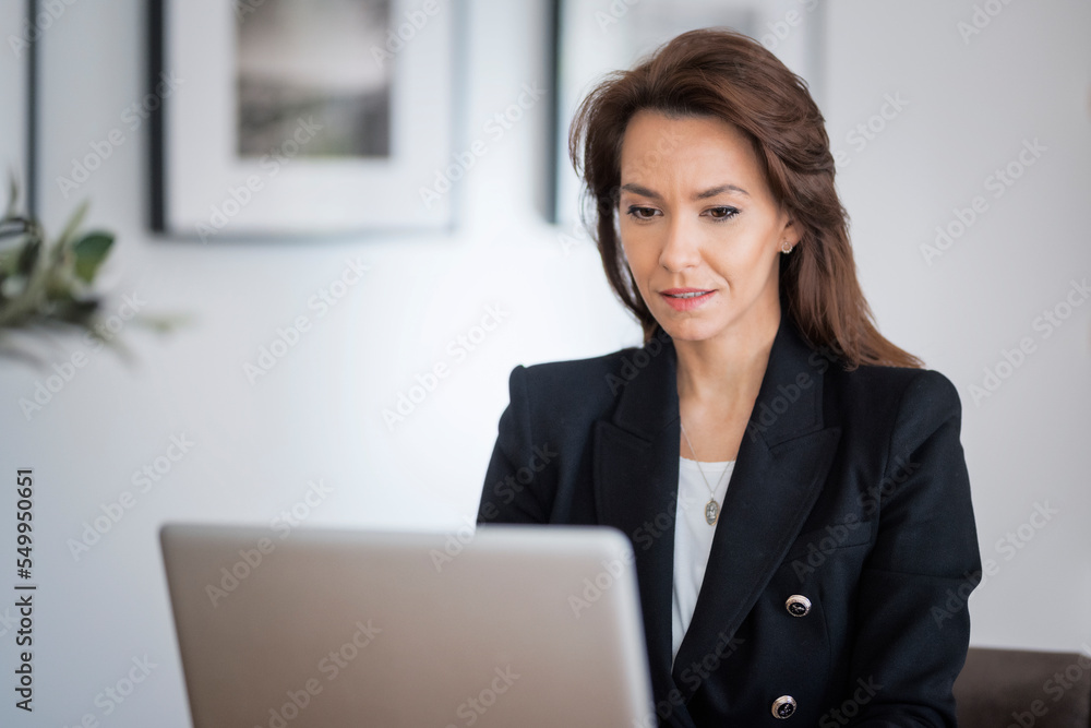 Happy middle aged woman sitting at tablet and using laptop while working at home Happy middle aged woman sitting at tablet and using laptop while working at home