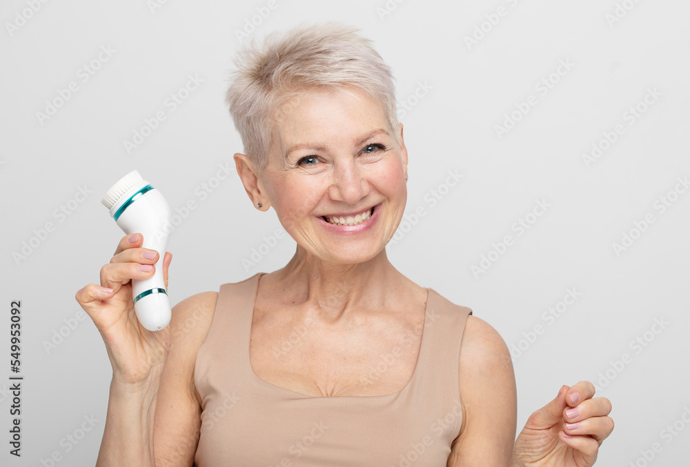 Beautiful 60s woman holding a massager in her hand. Spa technique skincare ads. Beautiful 60s woman holding a massager in her hand. Spa technique skincare ads.