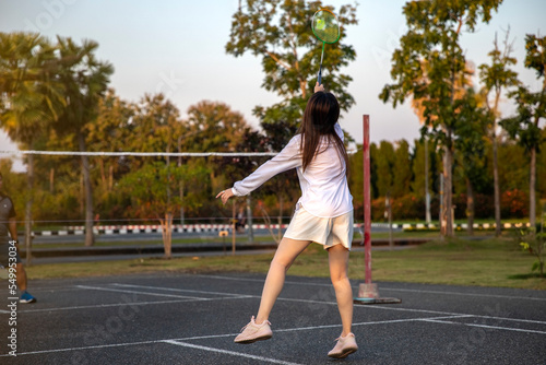 woman playing badminton in the park. urban asian sporty female having fun outdoor sports and game activity concept. © aumnat