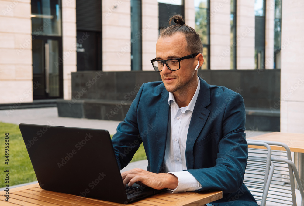 Young stylish man working on laptop computer while sitting at a cafe outdoors Young stylish man working on laptop computer while sitting at a cafe outdoors
