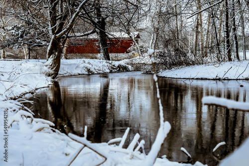 This covered bridge is covered with fresh snow, with the reflection on the creek in front of it 