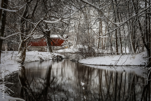 This covered bridge is covered with fresh snow, with the reflection on the creek in front of it 