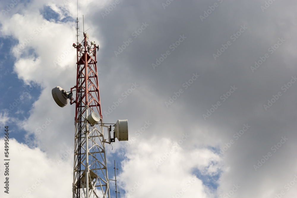 Telecommunication tower with radio, microwave and television antenna system located in the forest against the blue sky. Antenna tower, view from the ground Telecommunication tower with radio, microwave and television antenna system located in the forest against the blue sky. Antenna tower, view from the ground