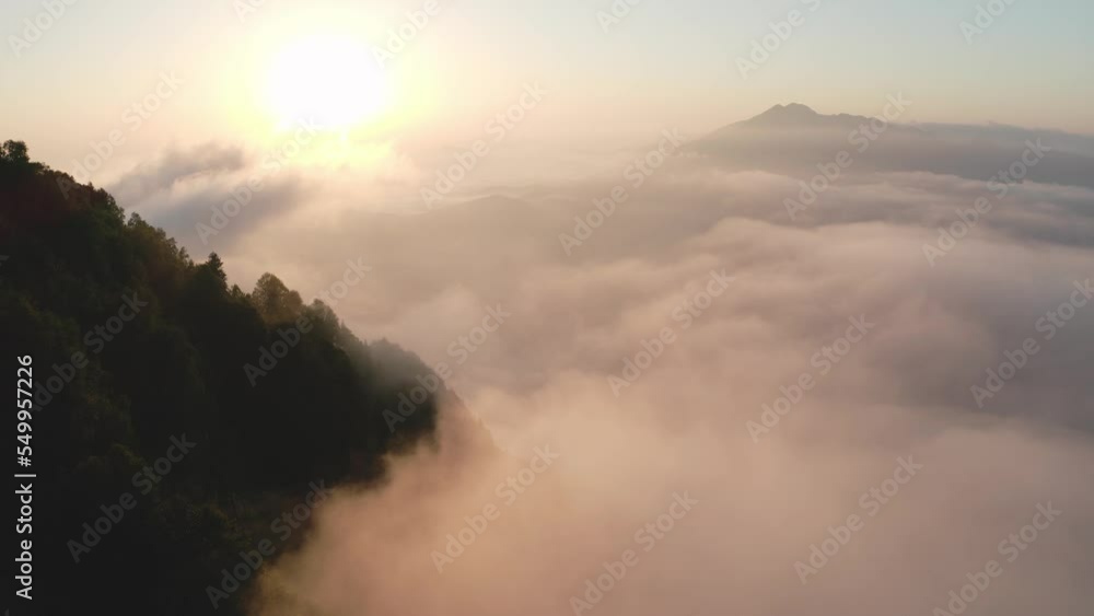 Aerial over heavy white cumulus clouds against clear sky bright orange sun and old distant mountain silhouettes in the evening, sunset time, panoramic view Aerial over heavy white cumulus clouds against clear sky bright orange sun and old distant mountain silhouettes in the evening, sunset time, panoramic view