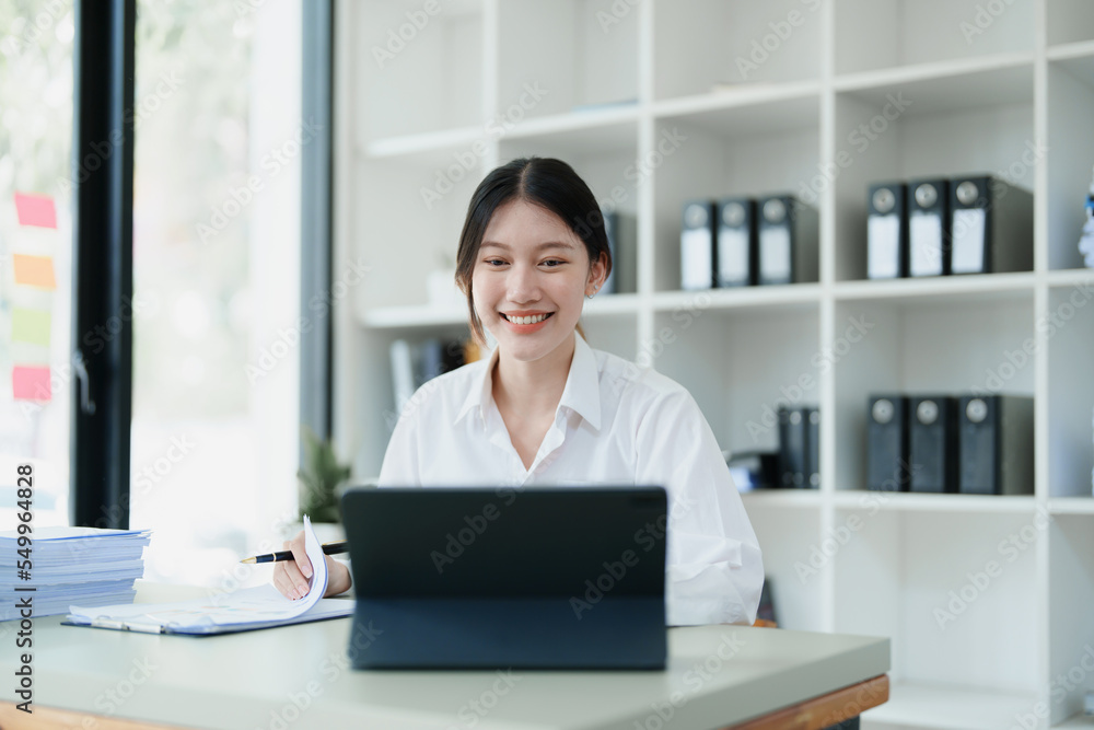Portrait of a thoughtful Asian businesswoman looking at financial statements and making marketing plans using a computer on her desk Portrait of a thoughtful Asian businesswoman looking at financial statements and making marketing plans using a computer on her desk