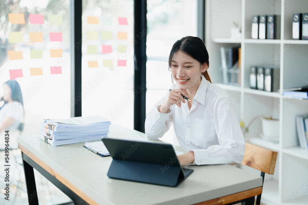 Portrait of a thoughtful Asian businesswoman looking at financial statements and making marketing plans using a computer on her desk Portrait of a thoughtful Asian businesswoman looking at financial statements and making marketing plans using a computer on her desk