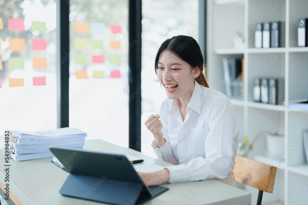 Portrait of a woman business owner showing a happy smiling face as he has successfully invested her business using computers and financial budget documents at work Portrait of a woman business owner showing a happy smiling face as he has successfully invested her business using computers and financial budget documents at work