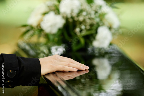 Close up of female hand on coffin saying goodbye at outdoor funeral ceremony, copy space photo