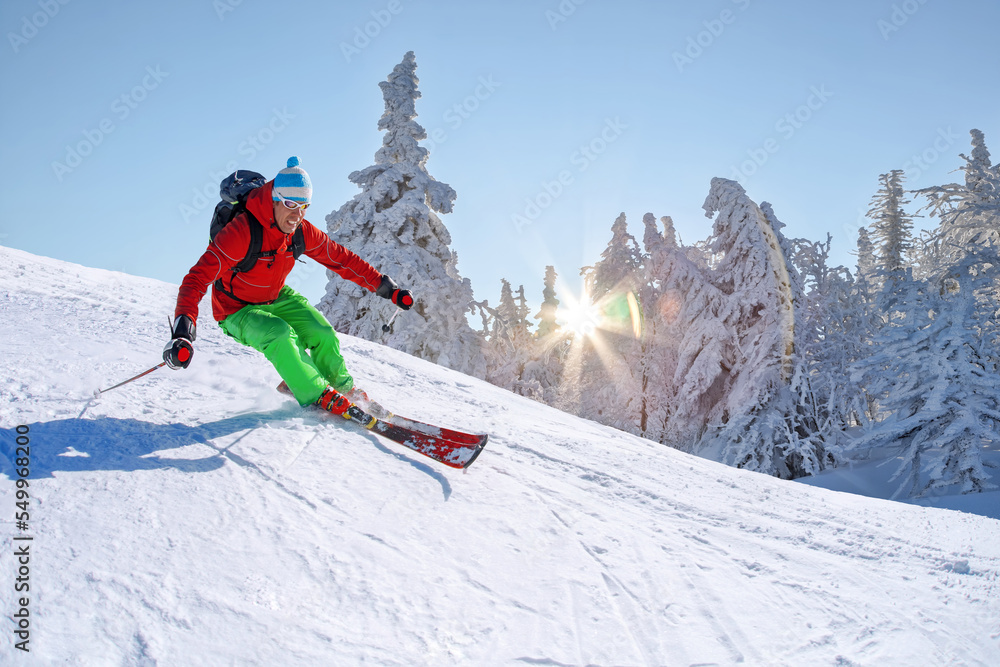 Skier skiing downhill in high mountains against against the fairytale winter forest with sunset.