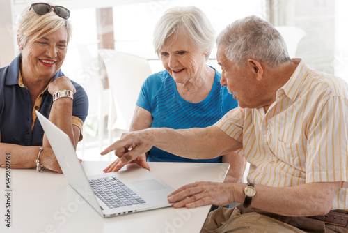 gruppo di tre anziani seduti comodamente intorno a un tavolino osservano lo schermo di un computer e l'uomo piu vecchio indica qualcosa.