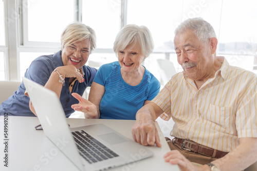 gruppo di tre anziani guarda sorridenti lo schermo di un computer seduti intorno a un tavolino