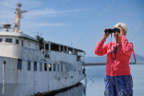 Donna con vestiti casual guarda dal binocolo vicino alla banchina di un porto 
