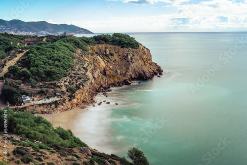 Nice cliff in the mediterranean sea near Sitges and Vilanova i la Geltru, spain. Long exposure photography on a sunny day overlooking the dead man's beach, horizontal. photo