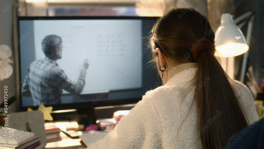 Young asian girl sits at the table at cozy room and learns new material. Schoolgirl listens online lesson of math and studies on pc. Mature teacher talks with student and shows equation on board Young asian girl sits at the table at cozy room and learns new material. Schoolgirl listens online lesson of math and studies on pc. Mature teacher talks with student and shows equation on board