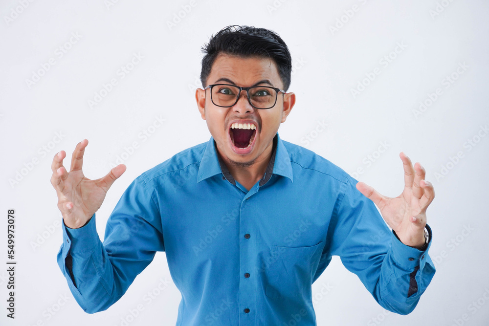 Annoyed handsome young asian man with glasses in wearing blue shirt raises palms while shouting loudly isolated on white background Annoyed handsome young asian man with glasses in wearing blue shirt raises palms while shouting loudly isolated on white background
