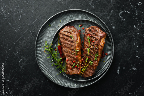 Grilled ribeye beef steak with rosemary, herbs and spices on a dark table. Free space for menus.