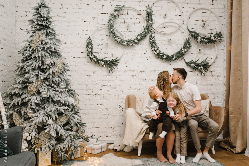 Merry Christmas. Happy mother, father, and kids near Christmas tree in home. Mom, dad hug children. Beautiful family enjoying their holiday time together and having fun. Decorated interior of a house.