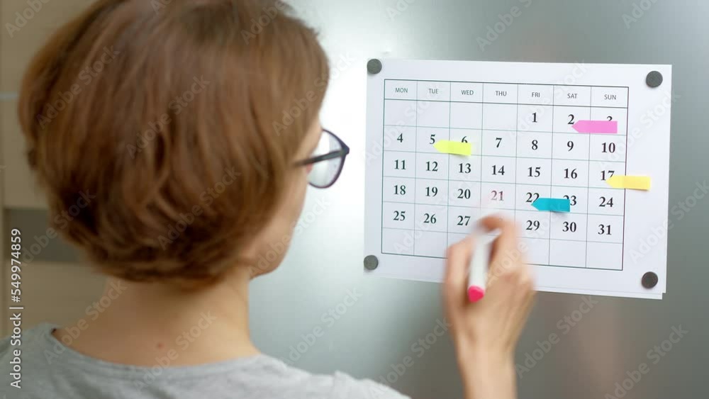 A woman marks the day on the calendar by planning a month for meetings and events. A woman marks the day on the calendar by planning a month for meetings and events.