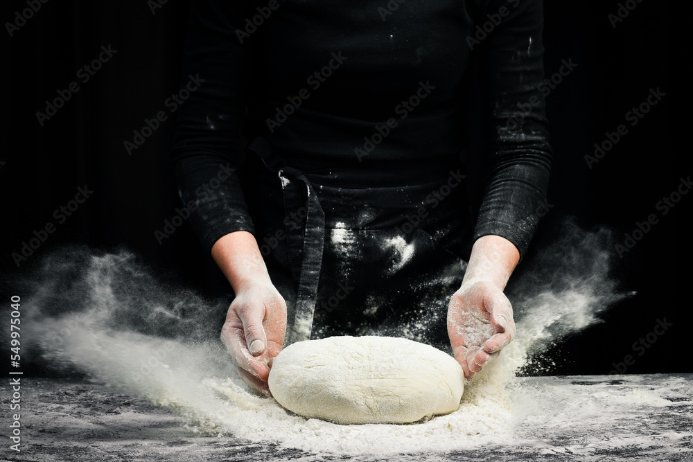 Fototapeta premium Cooking dough by chef hands for homemade pastry bread with flour splash. On a dark background.