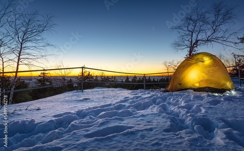 Yellow tent in front of a forest next to a wooden fence at sunset on a cold winter day photo