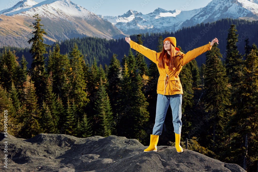 Woman in full height smile with teeth happiness hiker in yellow raincoat jumping up with his hands up on the mountain trip in the fall and hiking in the mountains in the sunset freedom