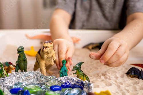 Closeup baby boy hands playing carnivorous and herbivorous dinosaurs with kinetic sand sensory box photo