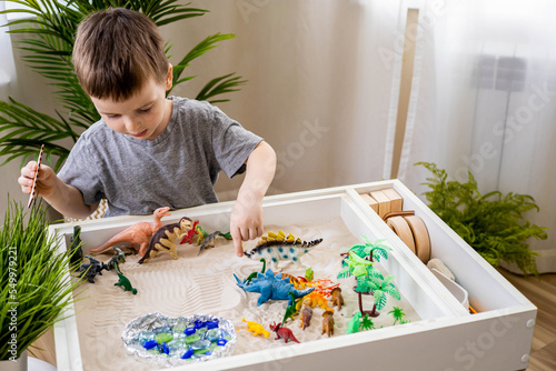 Cute baby boy playing sensory box kinetic sand table with carnivorous and herbivorous dinosaurs photo