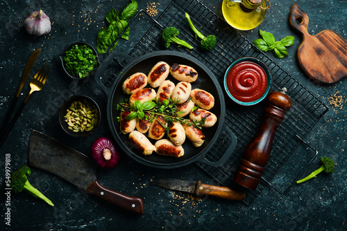 Mini grilled sausages on a frying pan. Barbecue. Meat menu. Top view. On a stone background.