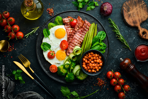 English breakfast: chickpeas, avocados, scrambled eggs, bacon vegetables on a black stone plate. Top view. Free space for text.