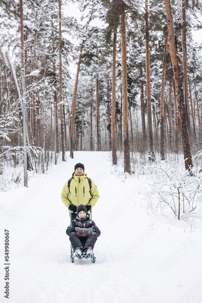 Father with backpack and little sos walking together in winter snowy forest. Happy man and joyful boy sledding and having fun together. Wintertime activity outdoors. Concept of local travel Father with backpack and little sos walking together in winter snowy forest. Happy man and joyful boy sledding and having fun together. Wintertime activity outdoors. Concept of local travel