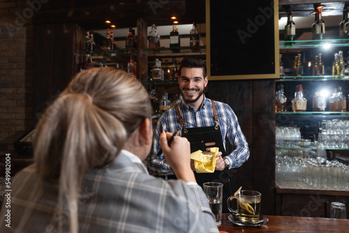 Quadro su tela Young lonely business woman sitting at the bar wooden counter working and talking with the bartender