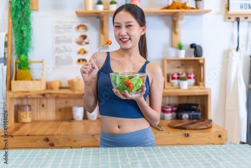 Young beautiful asian female adult lady in gym outfit after yoga exercise. Eat clean food salad with tomato for healthy and slim fit lifestyle.
