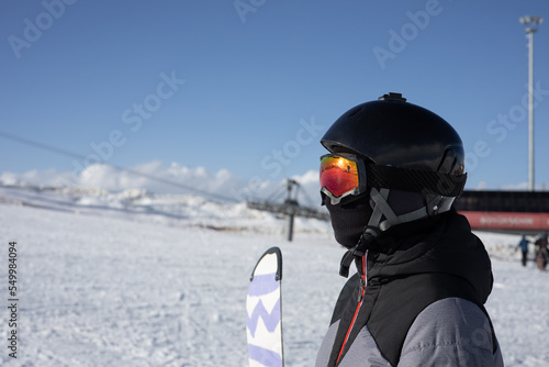 Girl or boy in ski helmet, sunscreen mask and balaclava with snowboard stands against the backdrop of snow-covered mountain ski slope and a cloudy sky. Winter. Sport and travel content   photo