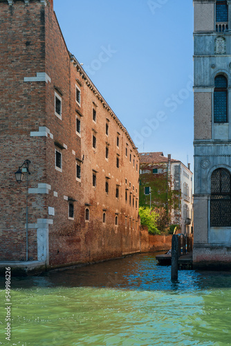 Brick walls of vintage houses on a narrow canal street in Venice on a sunny day, blue sky over Venetian houses, Venice city canal. Tourist travel in Italy. Vertical Orientation