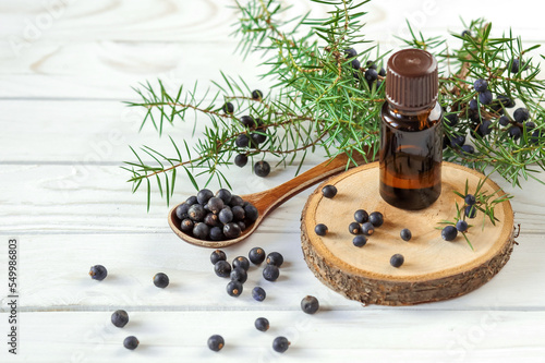 Fresh organic juniper berries in a wooden spoon and a bottle of oil on a white background