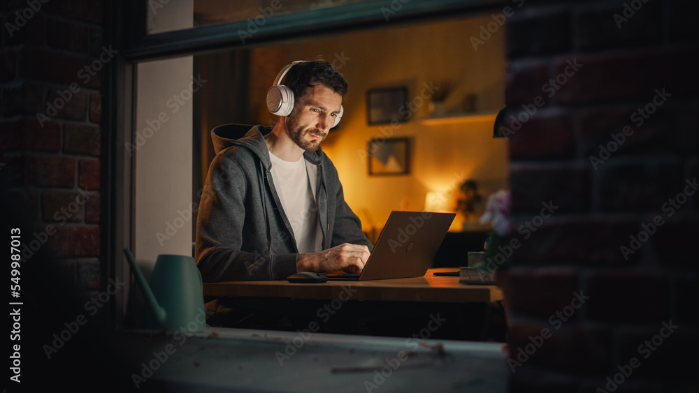 Professional Software Engineer Working From Home Office. Tired IT Specialist Feeling Sleepy and Finising Important Project. Application Development Process. View From Outdoors into Window. Professional Software Engineer Working From Home Office. Tired IT Specialist Feeling Sleepy and Finising Important Project. Application Development Process. View From Outdoors into Window.