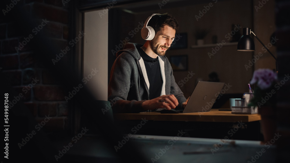 Happy Software Developer Working on a Laptop. Cheerful Information Technology Specialist Wearing Headphones, Listens to Music, Does Professional Work. Remote Job at Home Office Concept. Happy Software Developer Working on a Laptop. Cheerful Information Technology Specialist Wearing Headphones, Listens to Music, Does Professional Work. Remote Job at Home Office Concept.
