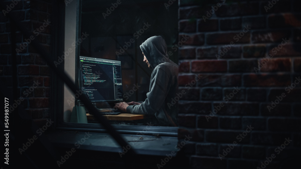 Night Apartment: Evil Male Hacker wearing Hoodie Breaks into Data Server Room, DDOS Attack, Phishing Scheme, Malware. Darknet Cyber Crime Concept. View From Outdoors into Window. - obrazy, fototapety, plakaty 