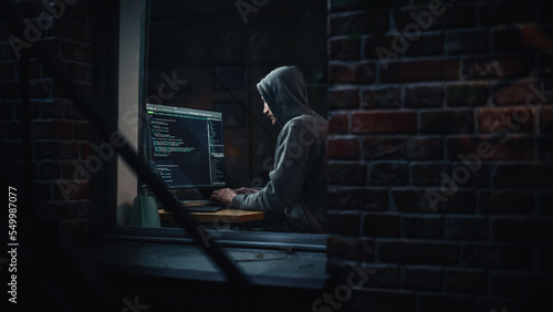 Night Apartment: Evil Male Hacker wearing Hoodie Breaks into Data Server Room, DDOS Attack, Phishing Scheme, Malware. Darknet Cyber Crime Concept. View From Outdoors into Window.
