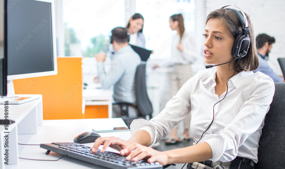 Beautiful friendly female customer support operator with headset using computer in call center Beautiful friendly female customer support operator with headset using computer in call center