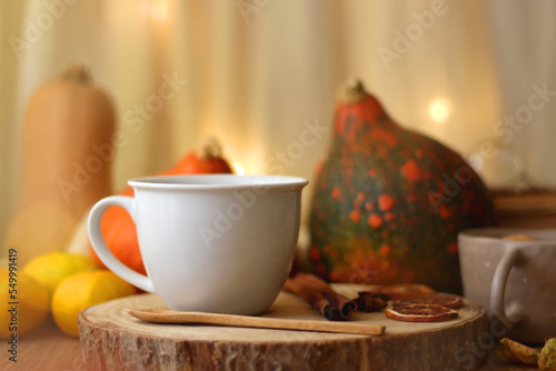 Fototapeta Naklejka Na Ścianę i Meble -  Cup of tea or coffee, seasonal spices, bowl of cookies, blanket, pumpkins, colorful leaves, books and tangerines on wooden table. Cozy hygge at home. Selective focus.