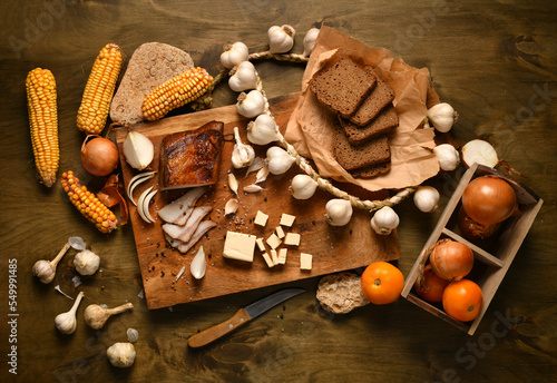 still life of food in a rural style on a dark wood background, lard and garlic, cheese, tomatoes and corn with rye bread, concept of fresh vegetables and healthy food