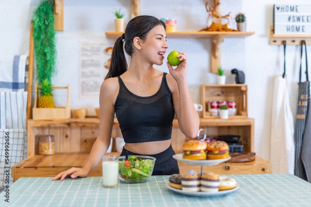 Young asian beautiful female lady in fitness costume say no to burgers and doughnuts, choose healthy milk and salad. Say no to cholesterol and junk food. Choose green apple. Healthy living