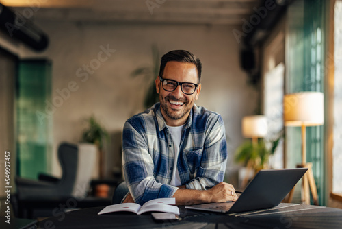 Businessman smiling for the camera, working over the laptop, usi