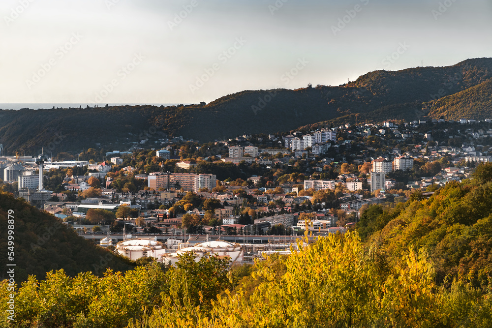 View from the height of the seaside town on a sunny autumn day. The mountains surrounding the town are covered with autumn vegetation under a blue cloudy sky.