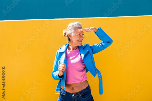 Smiling mature woman shielding eyes in front of colored wall